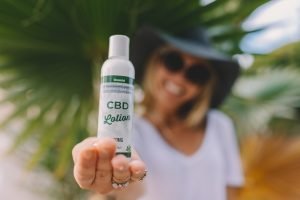 woman in hat holding CBD lotion to camera
